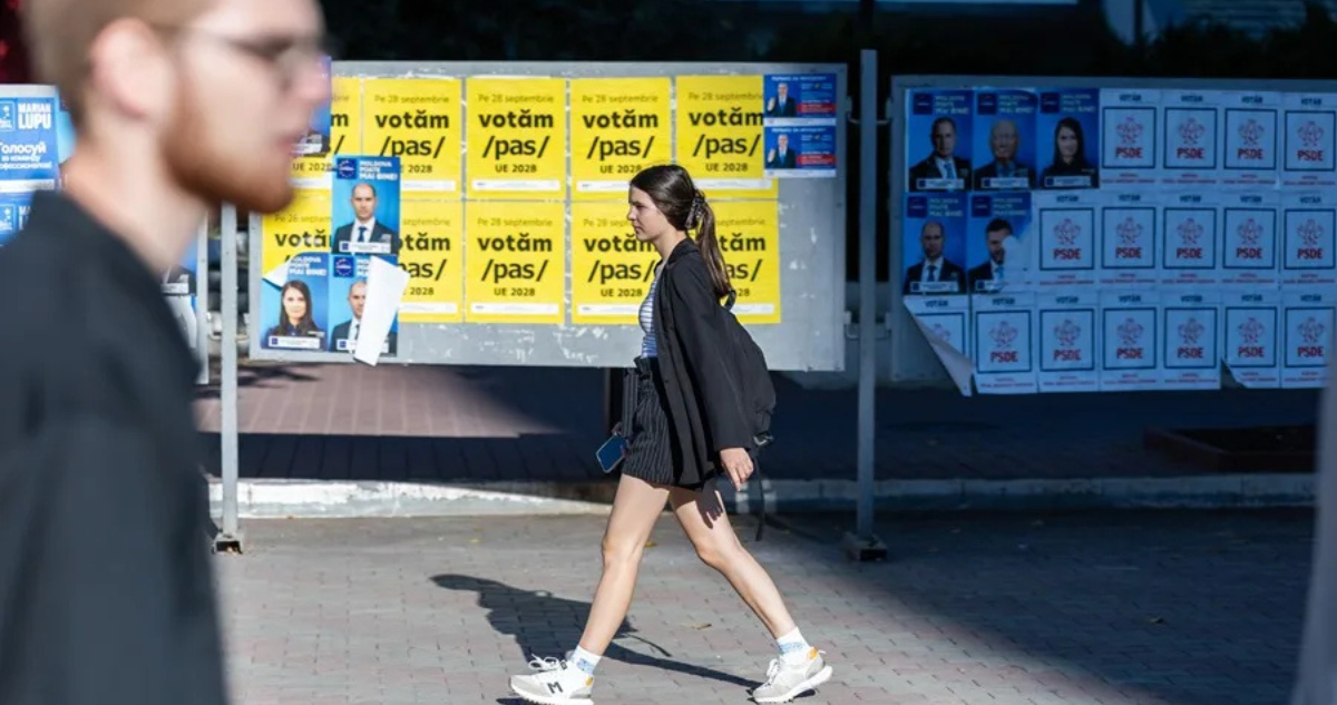 Dos jóvenes caminan junto a un panel cubierto de pósteres electorales, este martes 23 de septiembre en Balti (Moldavia).