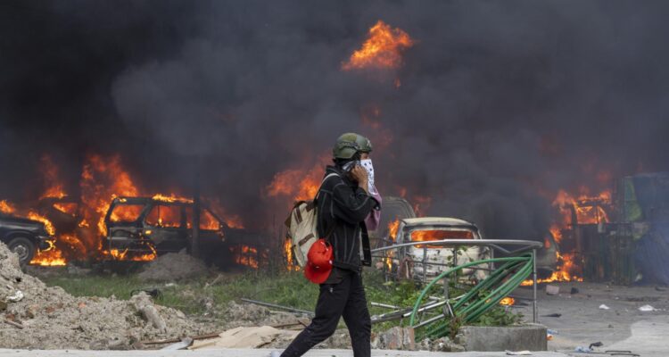 Un hombre camina cerca de vehículos en llamas frente al edificio de la Corte Suprema en Katmandú