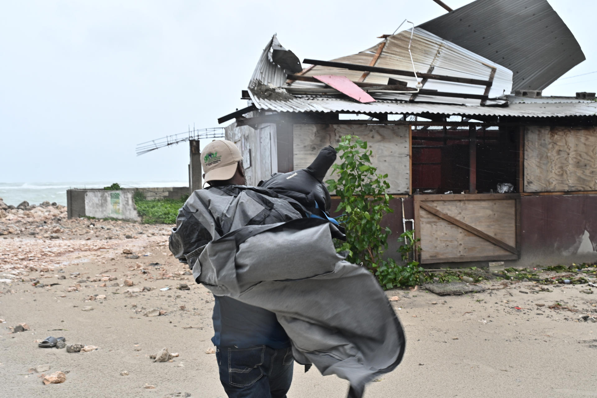 Un hombre carga una lona para cubrir el techo de una casa antes del paso de Melissa en la playa pesquera de Hellshire, Jamaica