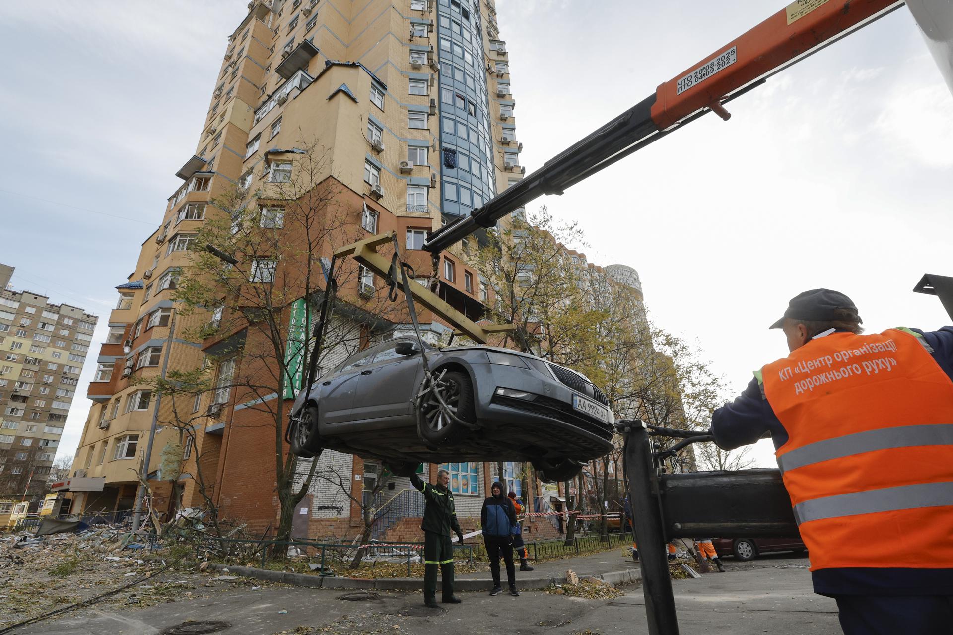 Trabajadores ucranianos retiran un automóvil dañado tras un ataque ruso contra un edificio residencial en Kiev
