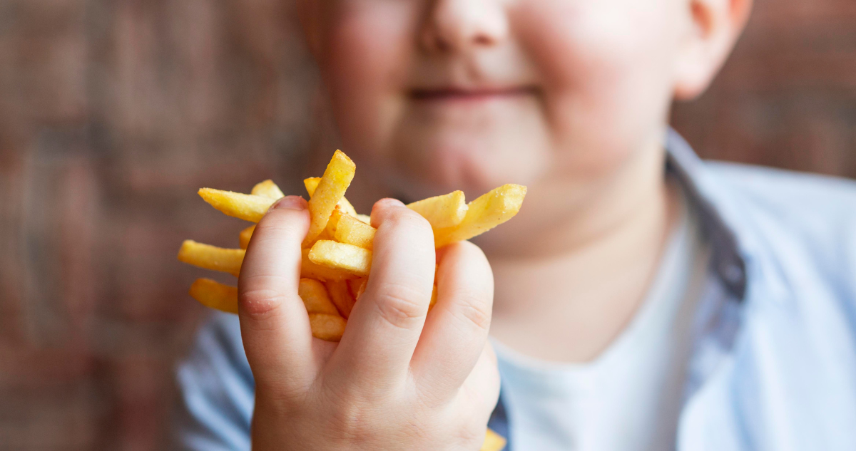 Foto de contexto de niño con obesidad comiendo papas fritas