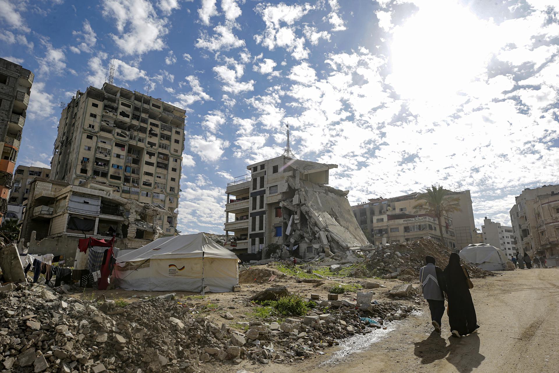 Palestinos caminan cerca de las ruinas de viviendas en la ciudad de Gaza