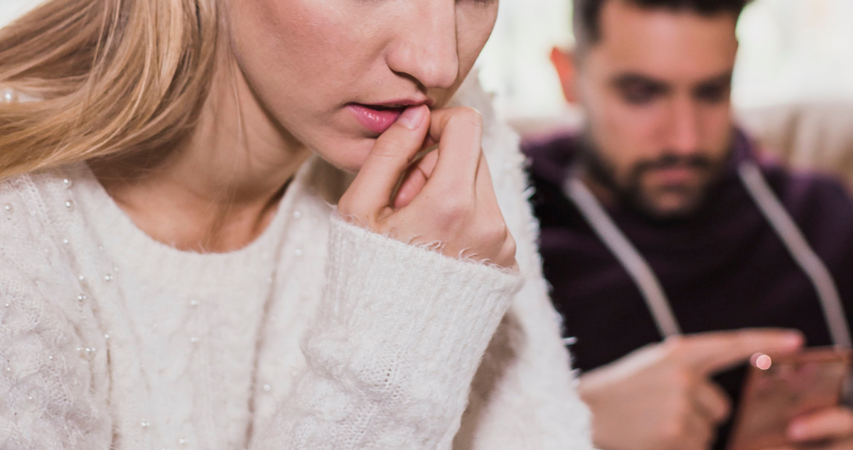 Foto de contexto de mujer con ansiedad mientras hombre mira su celular