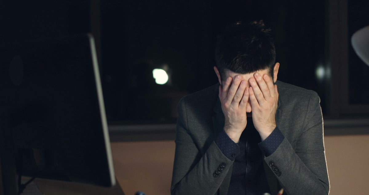 Persona agobiada tapándose el rostro mientras trabaja frente a un computador