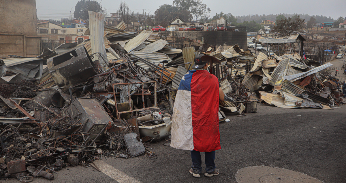 Hombre con una bandera chilena frente a viviendas destruidas por incendios en Punta de Parra, región del Bío Bío.
