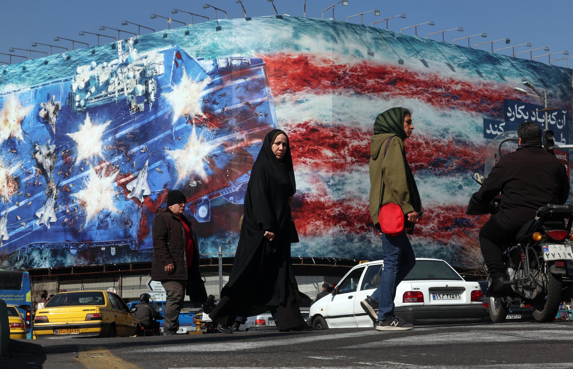 Iraníes pasan junto a un cartel publicitario antiestadounidense en la Plaza de la Revolución de Teherán, Irán