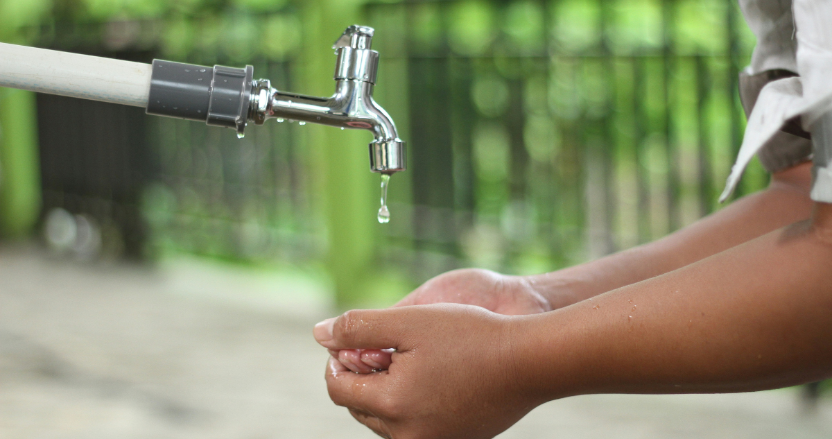 Manos de niño y gota de agua saliendo del grifo