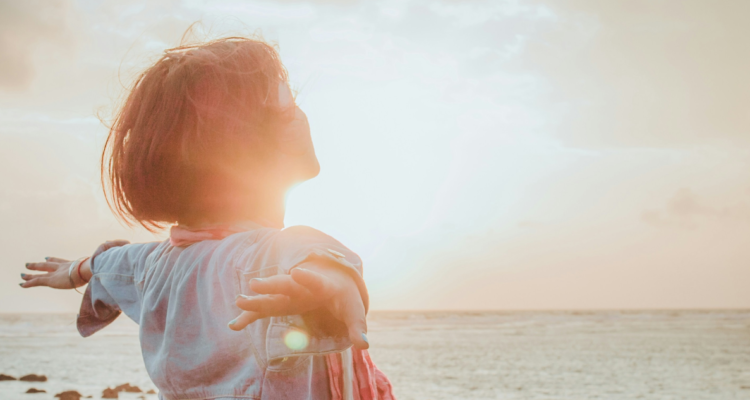 Persona feliz mirando el mar, iluminada por el sol