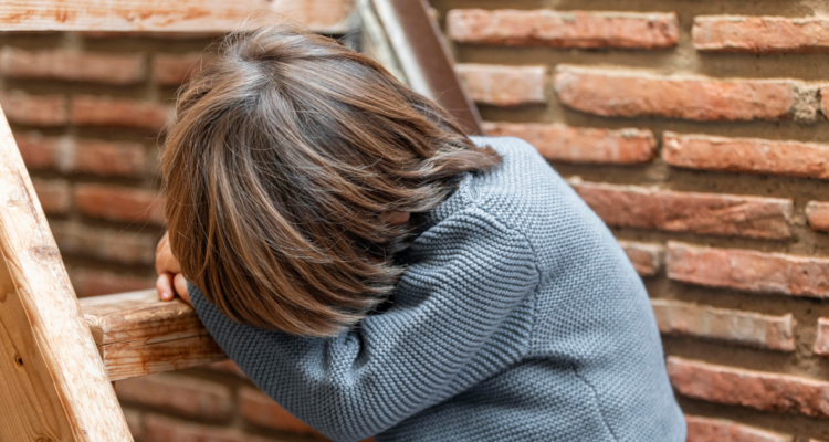 Niño con chaleco gris, sentado en una escalera, ocultando el rostro