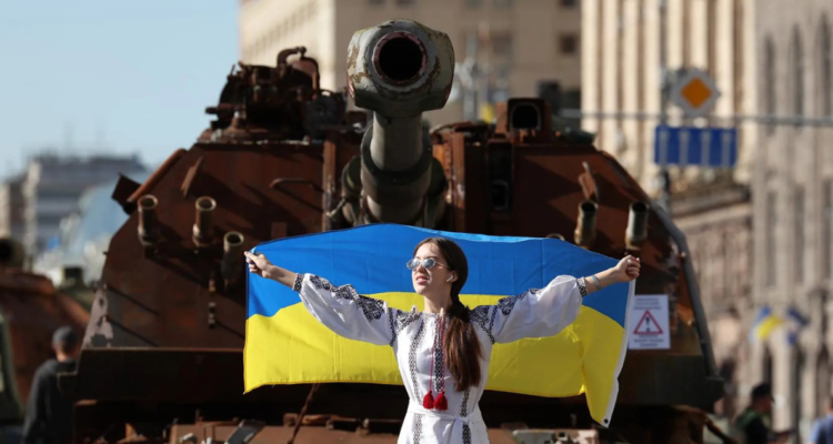Foto de contexto de una mujer con bandera ucraniana frente a un tanque