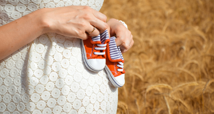 Mujer embarazada sosteniendo zapatitos de bebé sobre su vientre.