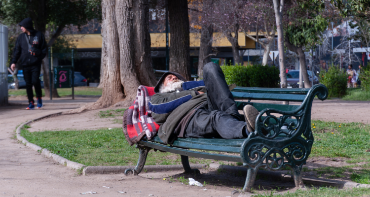 Persona en situación de calle acostada en una banca de un parque