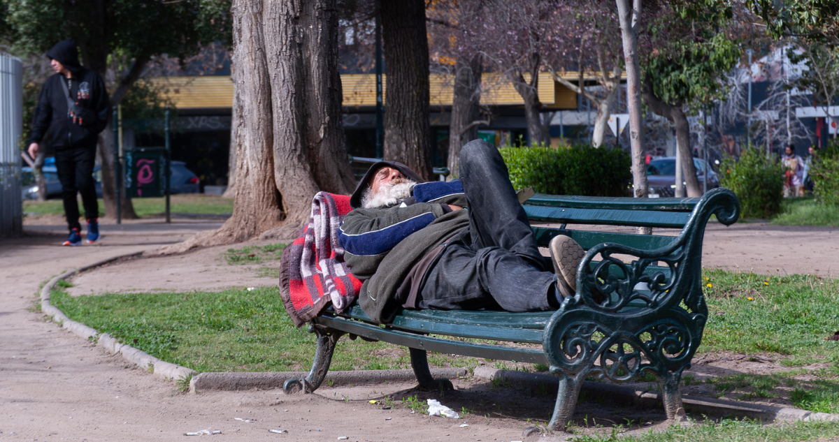 Persona en situación de calle acostada en una banca de un parque