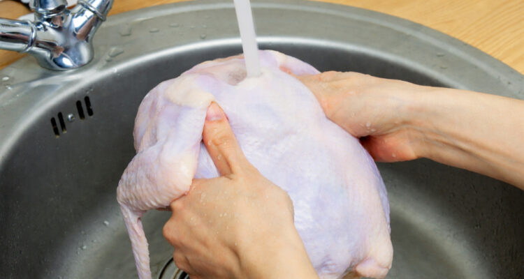 Foto de unas manos lavando un pollo bajo el grifo