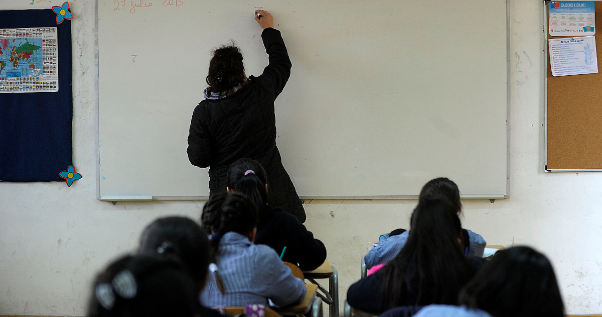 Niños en sala de clases y profesora escribiendo en el pizarrón.