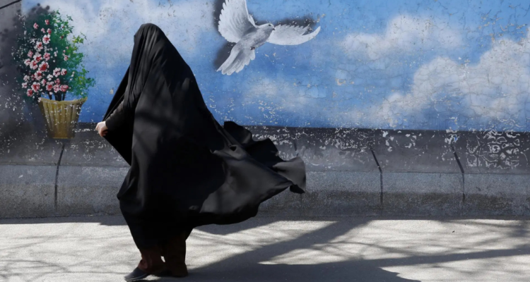 Mujer con burka caminando frente a muralla que tiene pintada una paloma y flores.