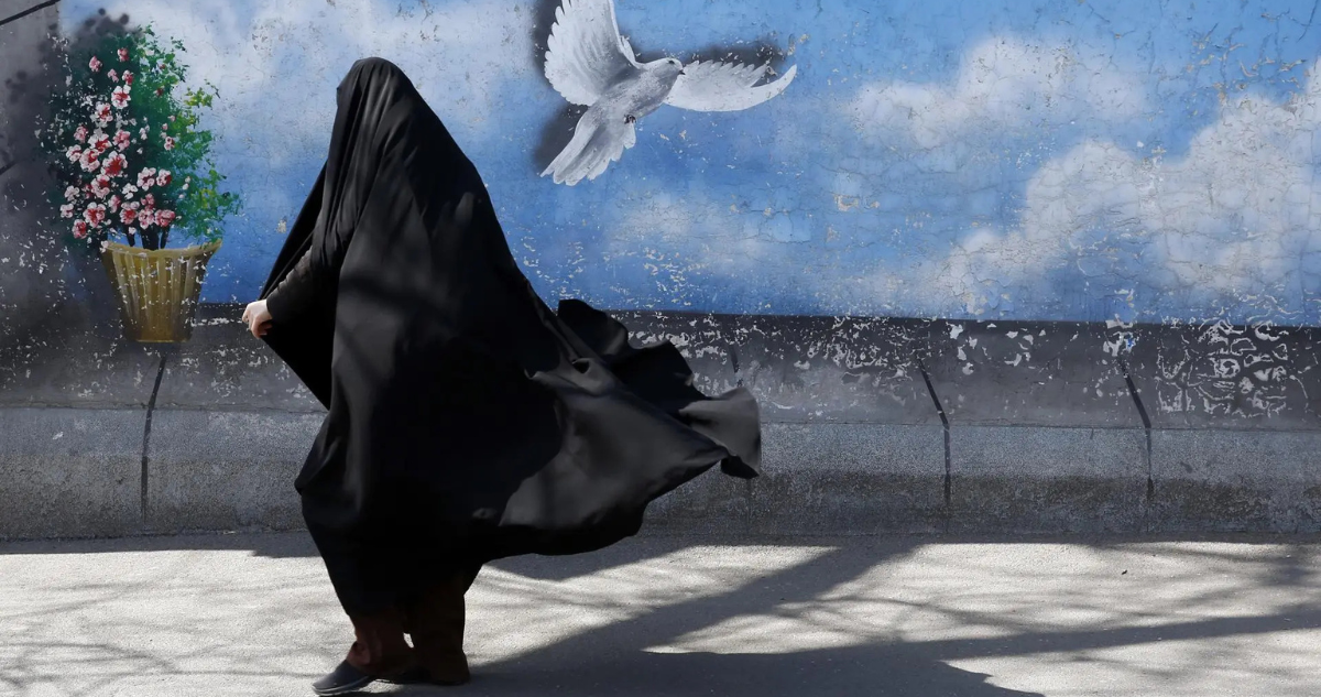 Mujer con burka caminando frente a muralla que tiene pintada una paloma y flores.