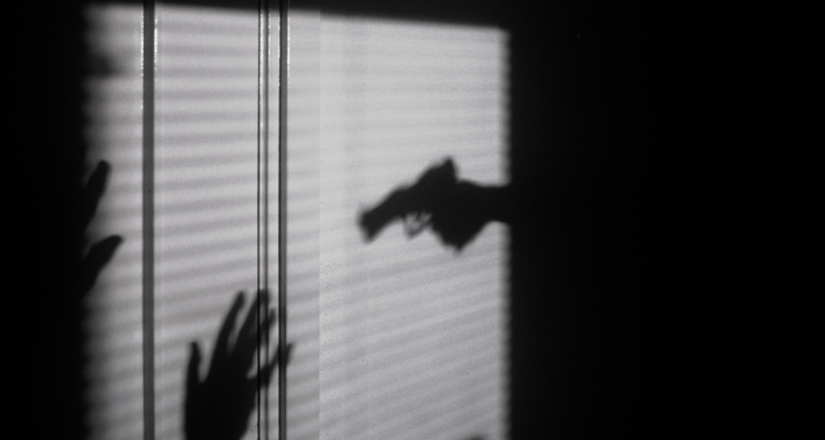 Sombra de persona apuntando a otra con un arma de fuego.