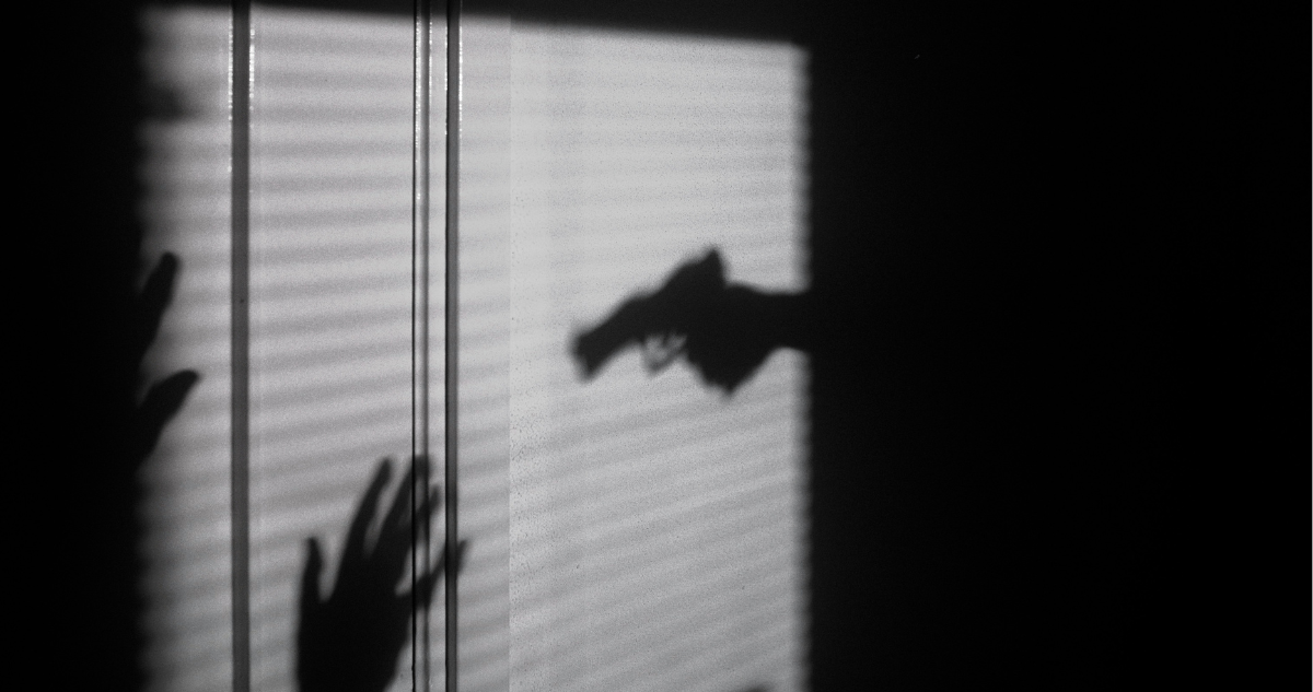 Sombra de persona apuntando a otra con un arma de fuego.