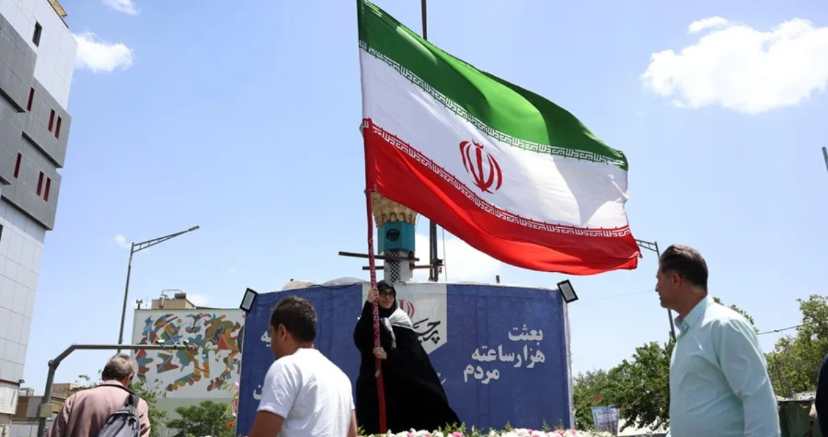 Personas caminan frente a una bandera de Irán en una calle de Teherán