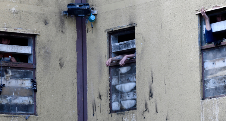 Brazos de personas privadas de libertad en ventanas de una cárcel.