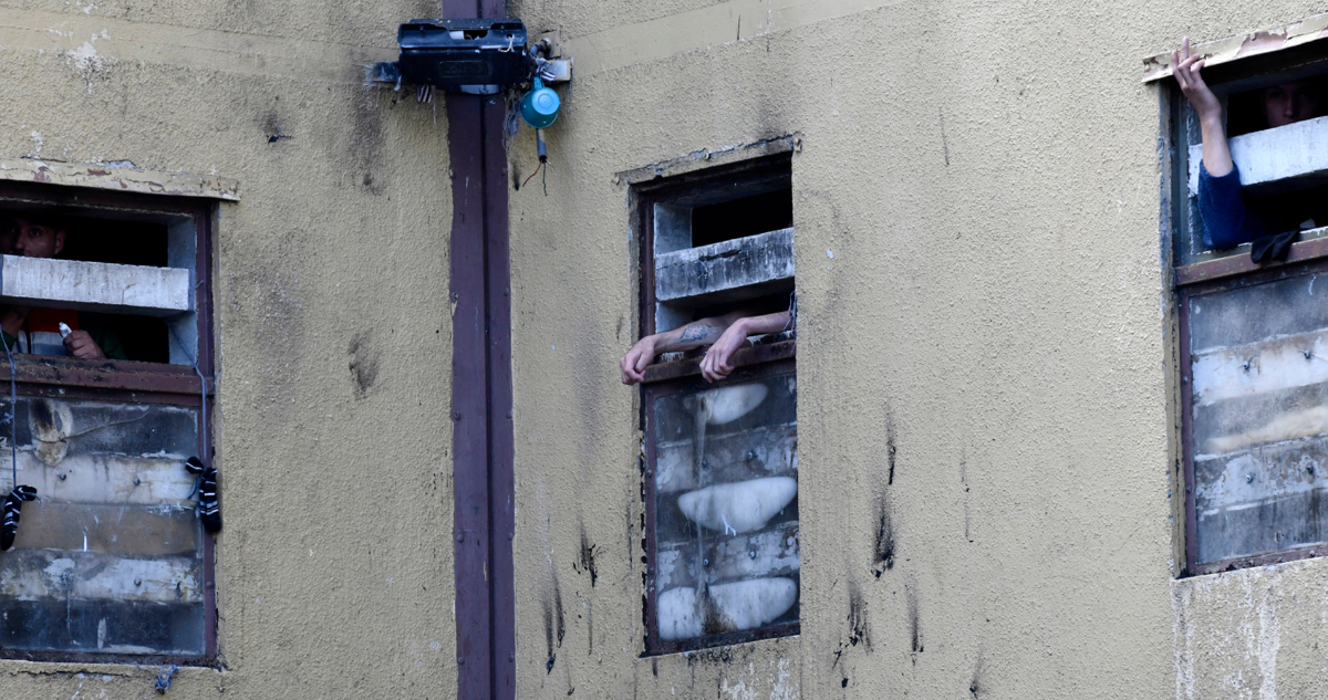 Brazos de personas privadas de libertad en ventanas de una cárcel.