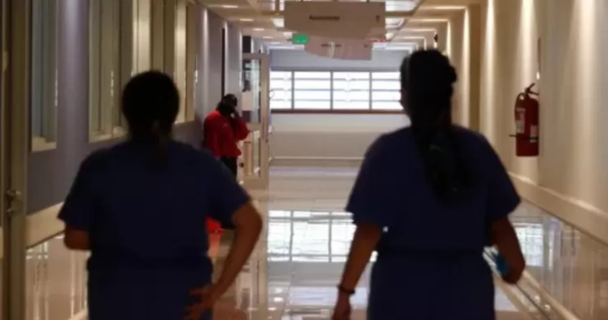 Personal de salud caminando por pasillo de recinto de salud.