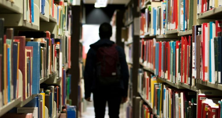 Estudiante caminando por pasillo de biblioteca de universidad.