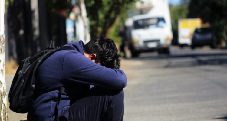 Escolar sentado en la vereda, con el rostro cubierto.