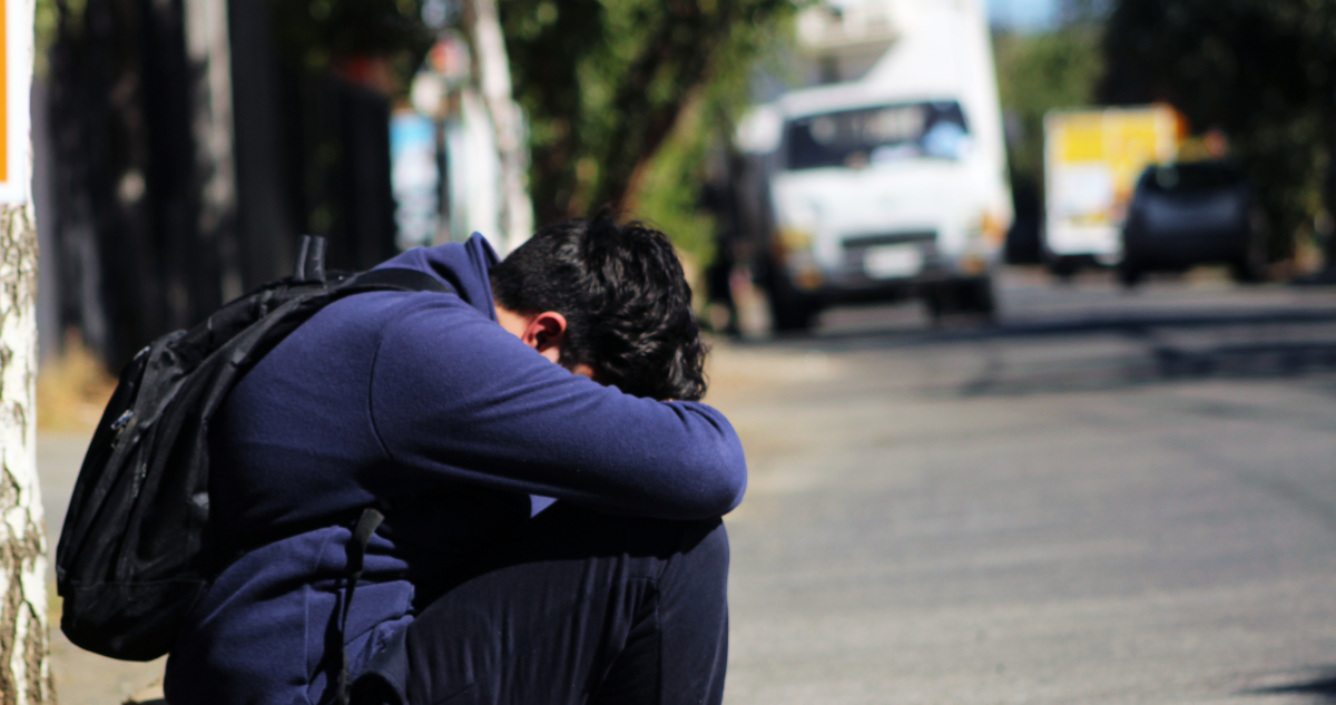 Escolar sentado en la vereda, con el rostro cubierto.