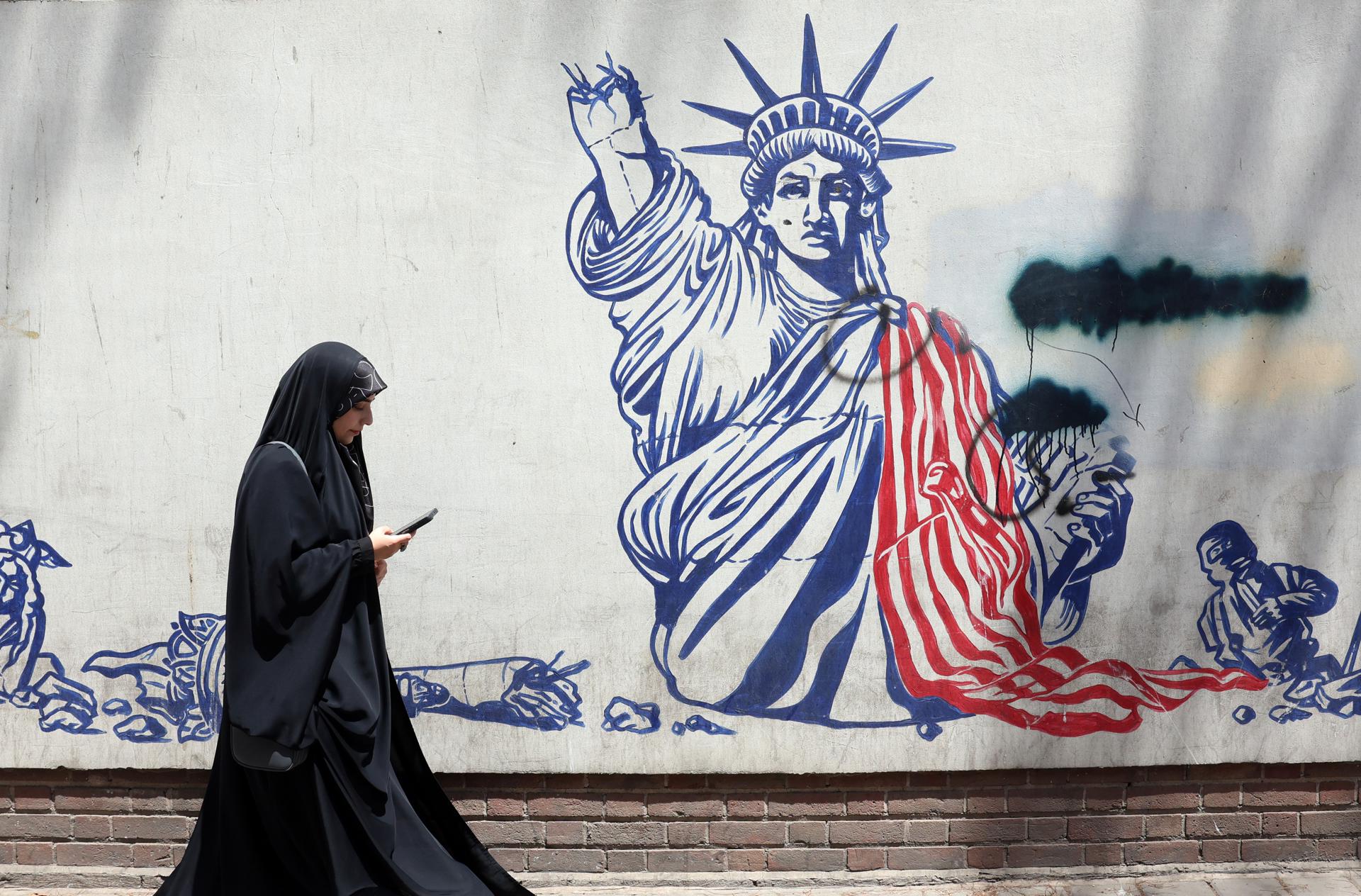 Una mujer camina frente a un mural anti EEUU junto a la antigua embajada estadounidense en Teherán