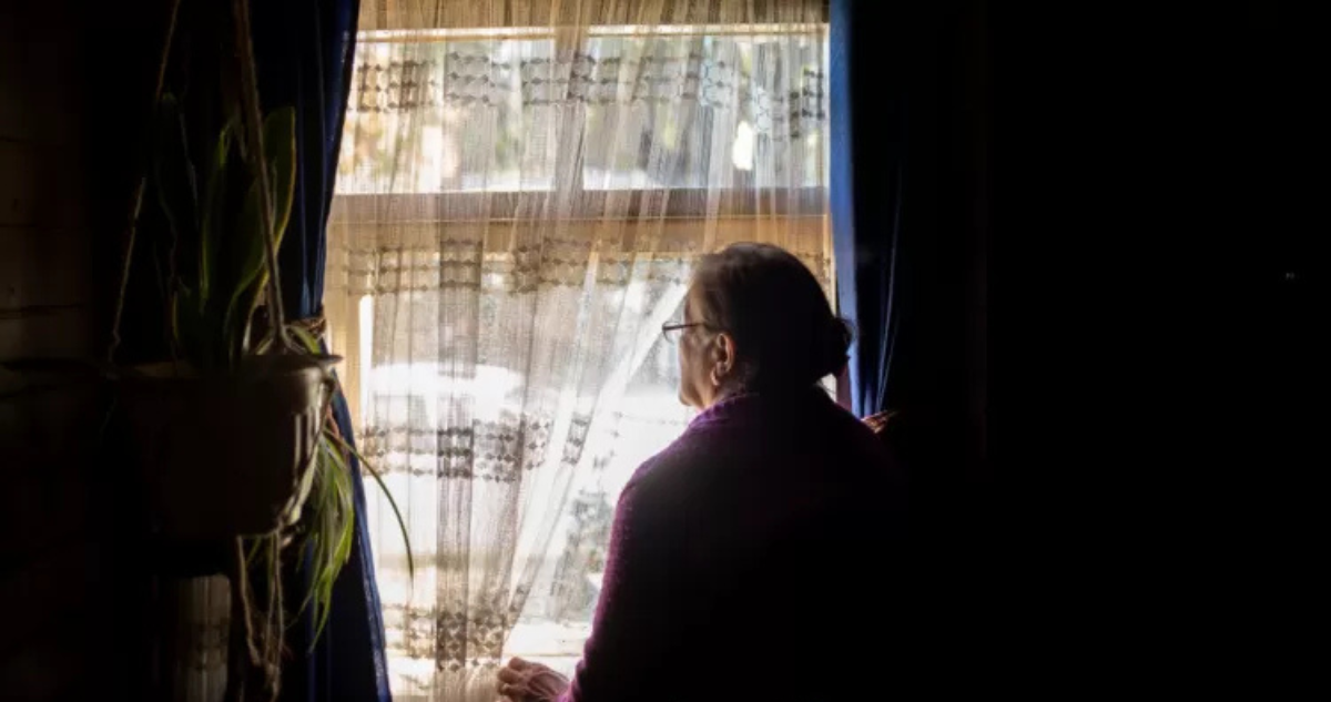Adulta mayor mirando por la ventana de su vivienda.