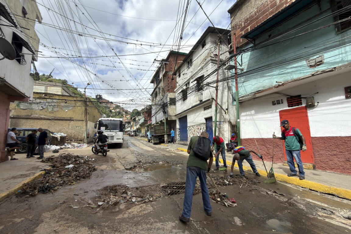 Personas limpian una calle tras las fuertes lluvias este domingo, en Caracas