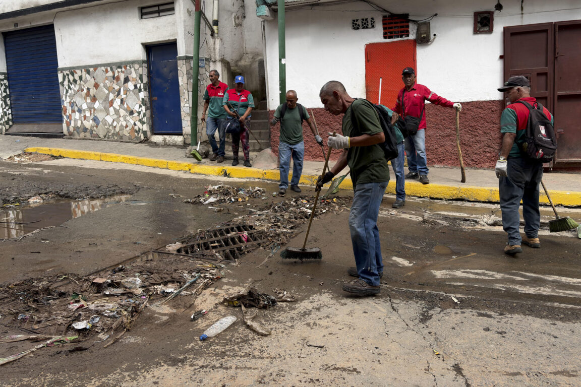 Personas limpian una calle tras las fuertes lluvias este domingo, en Caracas