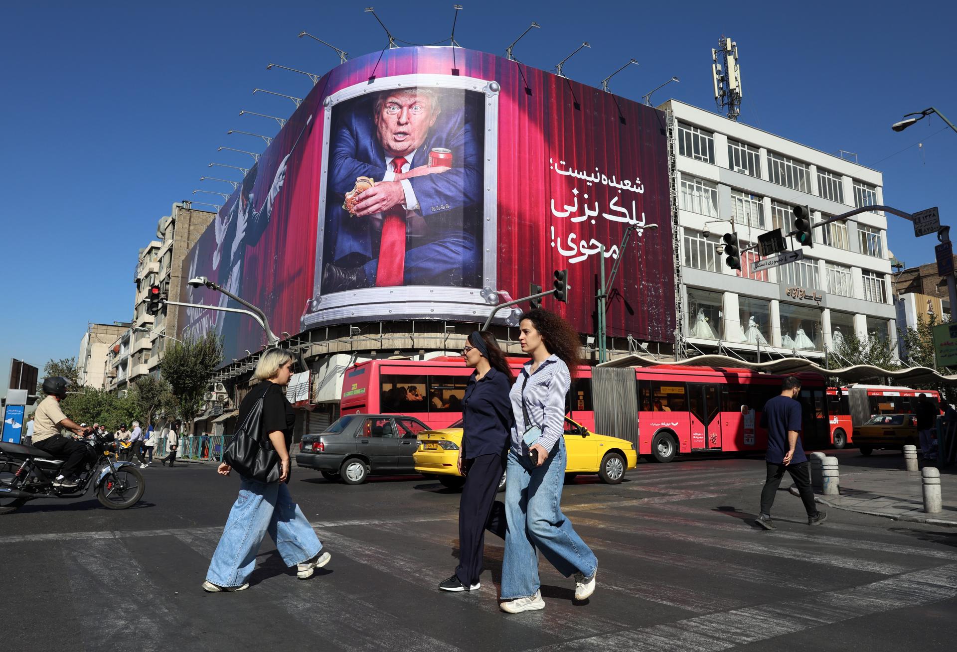 Iraníes pasan junto a un cartel anti-Trump en una calle de Teherán, Irán